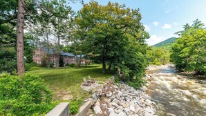 A riverside view with a house, a grassy area, and a rocky riverbank. - Entire Boutique Inn, Riverfront, 7 private suites (Intervale)