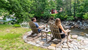 Two people seated at a table with chairs, a bottle of wine, and a stream in the background. - Entire Boutique Inn, Riverfront, 7 private suites (Intervale)