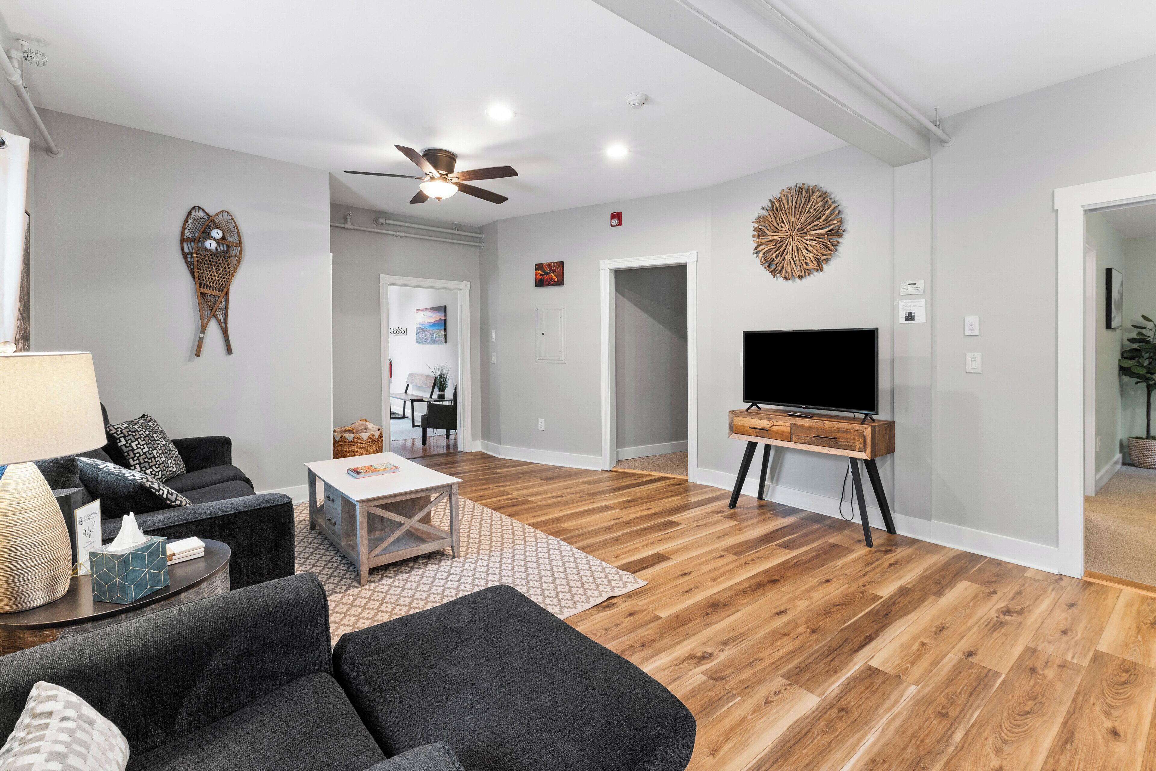 Ein modernes Wohnzimmer mit Fernseher, dunklen Sofas, einem Couchtisch und Deckenventilator.