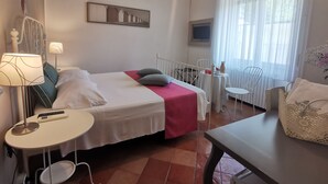 A hotel room with a bed, bedside tables, a small table, a chair, a window with curtains, and a wall-mounted air conditioner.