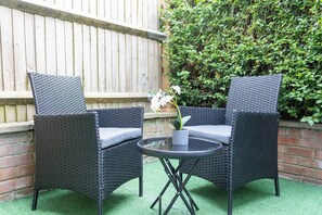 Twee rieten stoelen met kussens, een ronde tafel en een potorkidee.