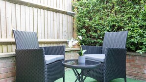 Two wicker chairs with cushions, a small round table, and a potted orchid. - Pleasant Studio in St Albans (St Albans)