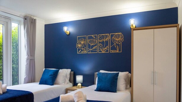 A hotel room with two beds, a wardrobe, and artwork on the wall.