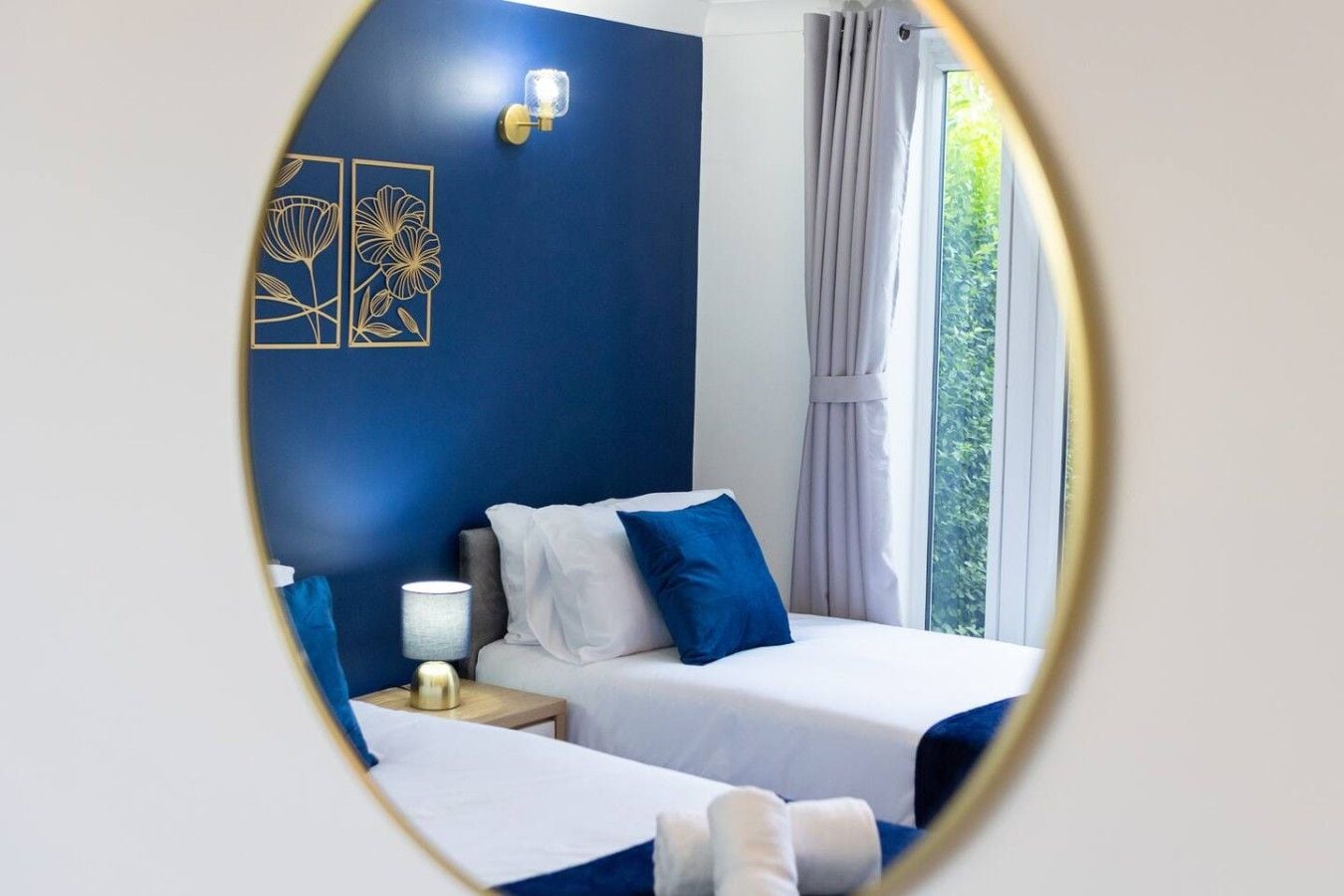 Ein Hotelzimmer mit zwei Betten, einem Nachttisch, einer Lampe und einer Wand mit floralem Dekor.