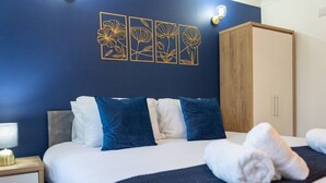 A hotel room with a bed, pillows, a nightstand, a wall art piece, and a wardrobe.