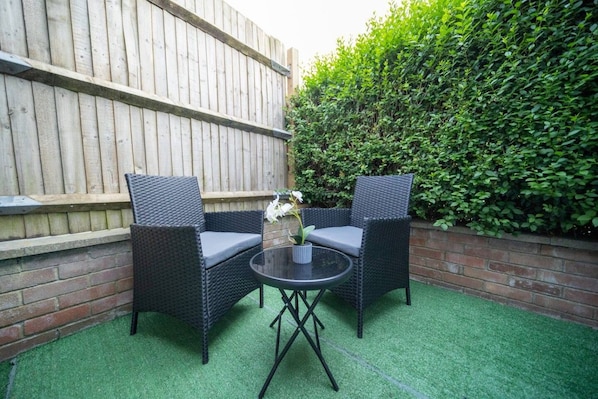 A patio area with two wicker chairs, a round table, and a potted plant.