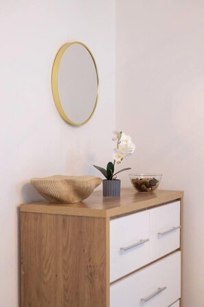 A wooden dresser with white drawers and a round mirror with a gold frame on the wall.