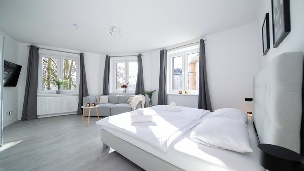A modern hotel room with a large bed, a sofa, a small table, and a TV. - Favorite Stays - Düsseldorf (Düsseldorf)