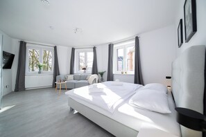 Una habitación de hotel moderna con una cama grande, un sofá, una mesita y un televisor.