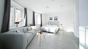 A modern bedroom with a large bed, a grey sofa, and a small round table with a tray. - Favorite Stays - Düsseldorf (Düsseldorf)