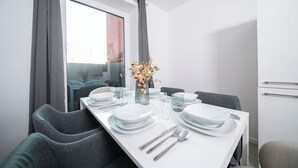 A modern dining area with a white table set for four, grey upholstered chairs, and a vase with flowers. - Favorite Stays - Düsseldorf (Düsseldorf)