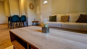 A living room with a wooden coffee table, a sofa with cushions, a dining table with chairs, and a door with a window. - A haven of peace near Pérouges, charm and comfort (Faramans)