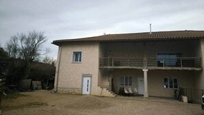 A two-story building with a balcony on the upper floor, a garage door, and a small front porch. - A haven of peace near Pérouges, charm and comfort (Faramans)