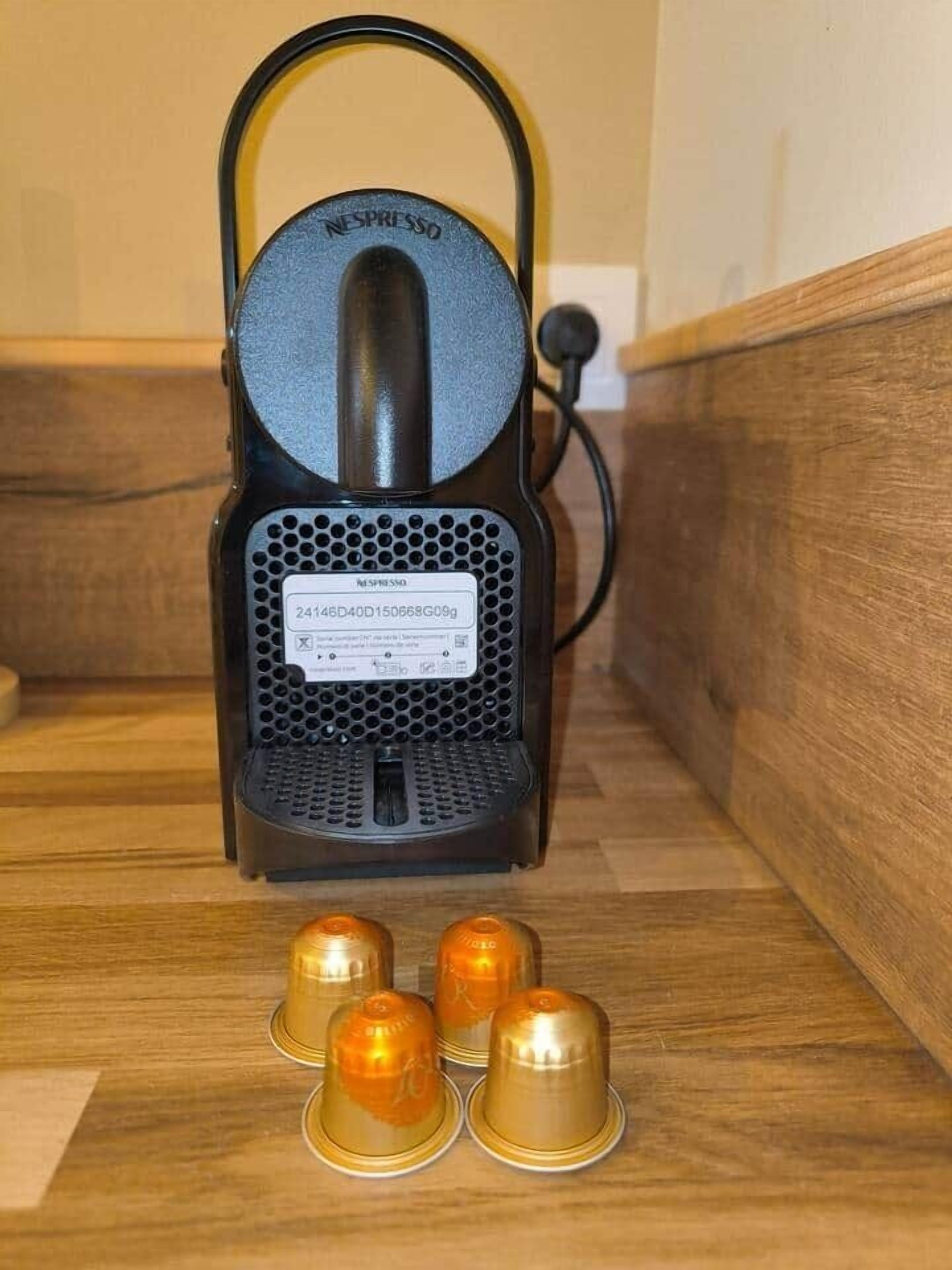 Een Nespresso koffiemachine met vier capsules op een houten ondergrond.