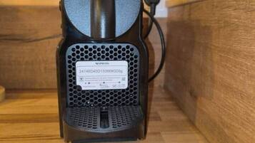 Een Nespresso koffiemachine met vier capsules op een houten ondergrond.