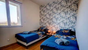 A bedroom with two beds, a large window, and a patterned wall. - A haven of peace near Pérouges, charm and comfort (Faramans)