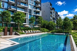 Un hotel moderno con piscina, sillones de descanso y un jardín bien cuidado.