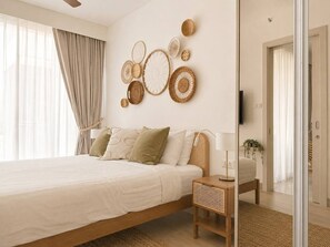 Un dormitorio moderno con una cama grande, una mesita de noche, un televisor montado en la pared y una puerta que da a otra habitación.