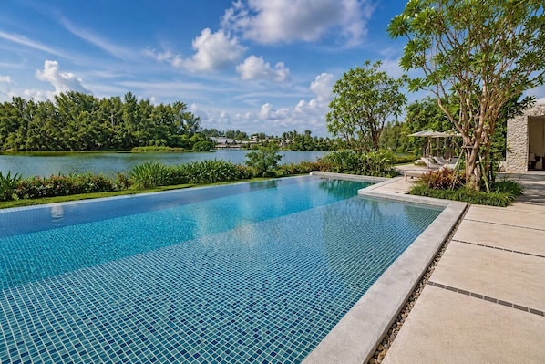 A clear blue infinity pool with a view of a lake and trees.