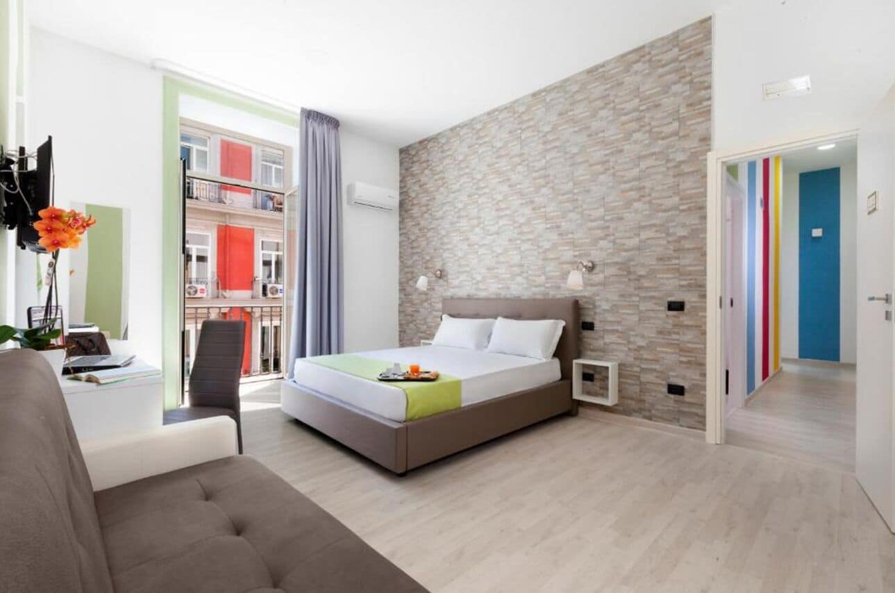 A modern hotel room with a bed, a desk, and a view of a balcony.