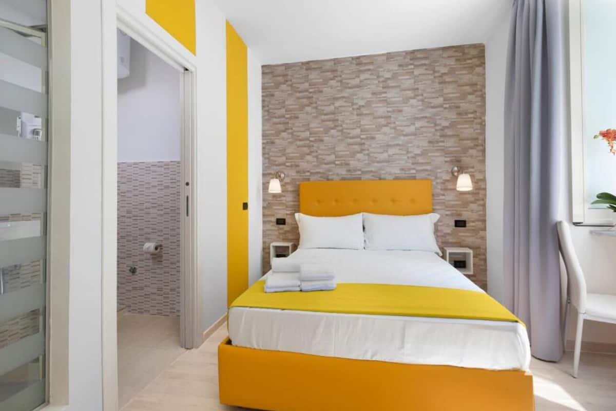 A hotel room with a bed, a nightstand, a chair, and a bathroom visible through an open door.