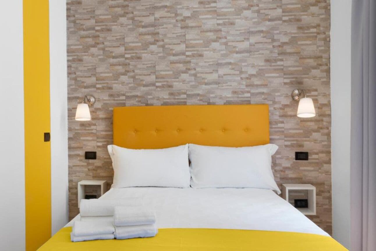 Een hotelkamer met een bed, twee nachtkastjes en een wand met een structuur.
