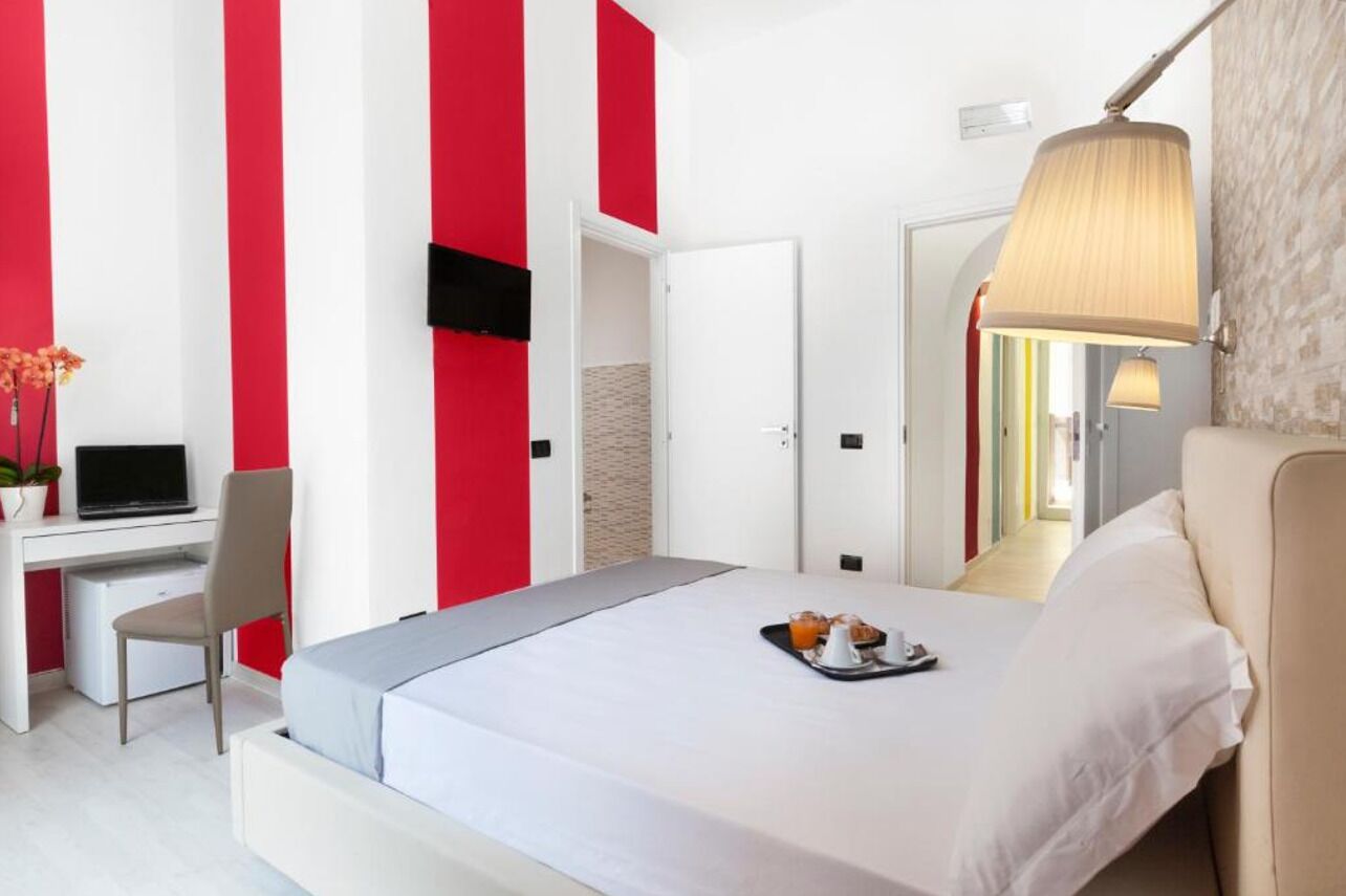 Habitación de hotel con cama, escritorio con una laptop, una silla y una bandeja con alimentos para el desayuno.
