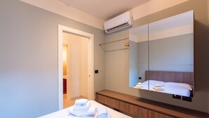 Ein modernes Hotelzimmer mit einem großen Bett, einem Holz-Kopfteil, einem eingebauten Fernseher und einer Wand-Klimaanlage.