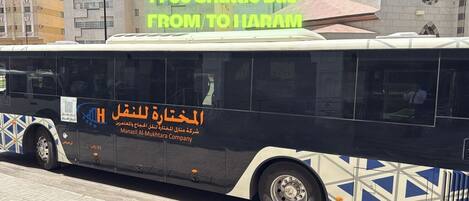 Een shuttlebus met de tekst 'Gratis shuttlebus NAAR VANDAAN HARAM' en de branding van 'Manazil Al-Mukhtar Company'.