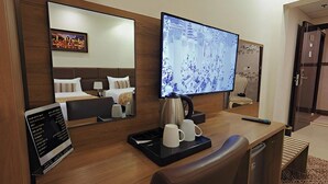 Habitación de hotel con un escritorio de madera, un televisor de pantalla plana, una cama con ropa blanca y una cafetera.