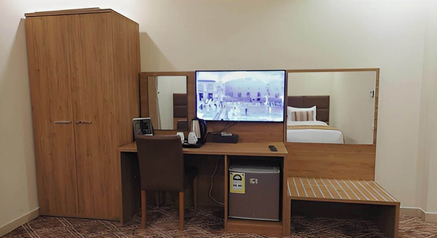 Ett kompakt hotellrum med ett skrivbord i trä, en tv, en säng och en garderob.