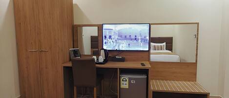A compact hotel room with a wooden desk, a television, a bed, and a wardrobe.