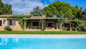 A poolside view of a stone house with a tiled roof, a patio with outdoor furniture, and lush greenery. - Villa 'Reco Vert' with Mountain View, Private Pool and Air Conditioning (Pollença)