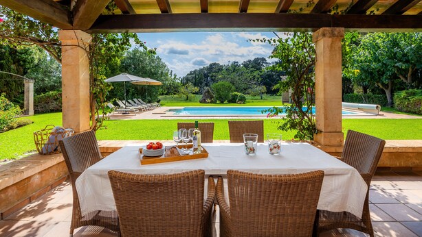 An outdoor patio with a table set for dining, overlooking a swimming pool and lush greenery. - Villa 'Reco Vert' with Mountain View, Private Pool and Air Conditioning (Pollença)