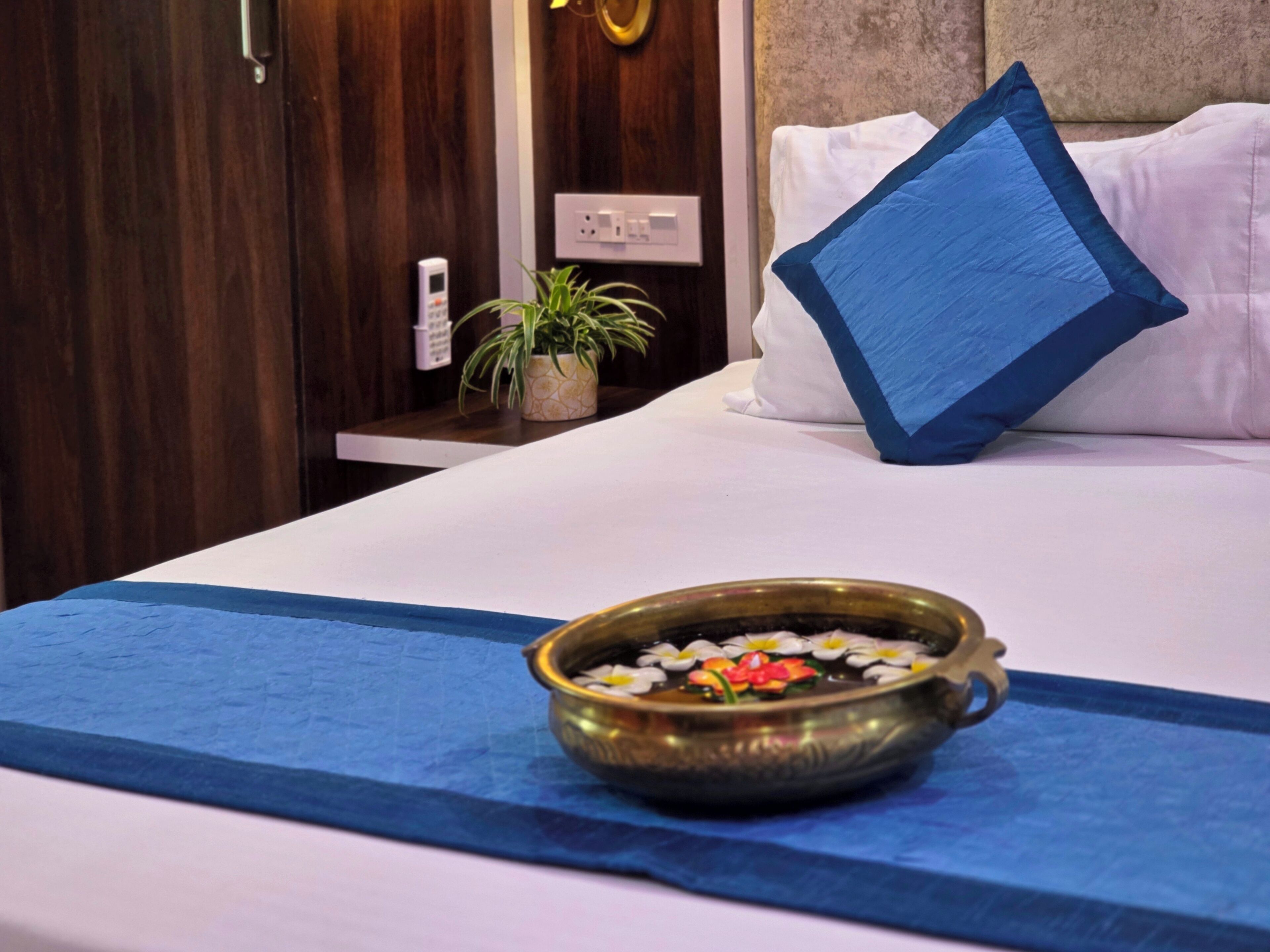 Cama bem arrumada com almofada azul e uma pequena tigela de flores sobre um tecido azul.