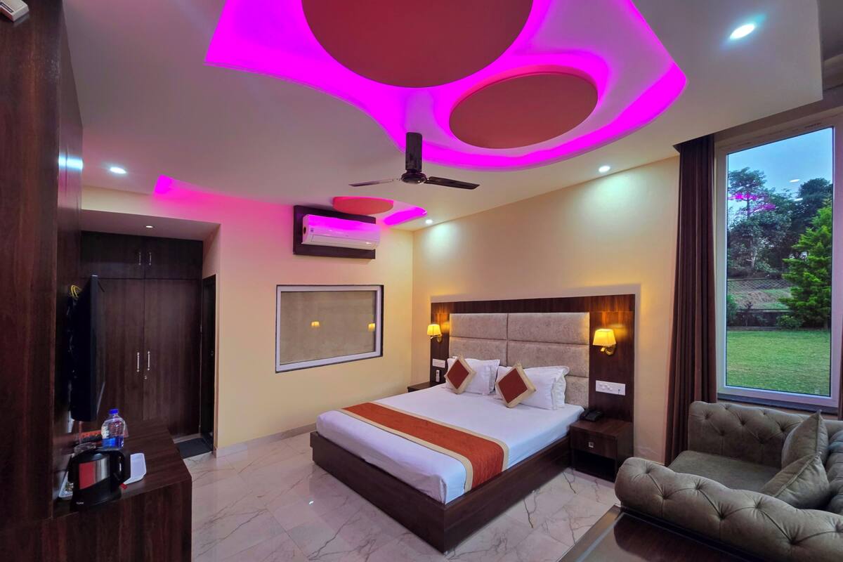 A modern hotel room with a large bed, a sofa, a TV, and a window with a view of the outdoors.