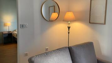 En moderne stue med en grå sofa, et rundt spejl, en gulvlampe og et indrammet kunstværk på væggen.