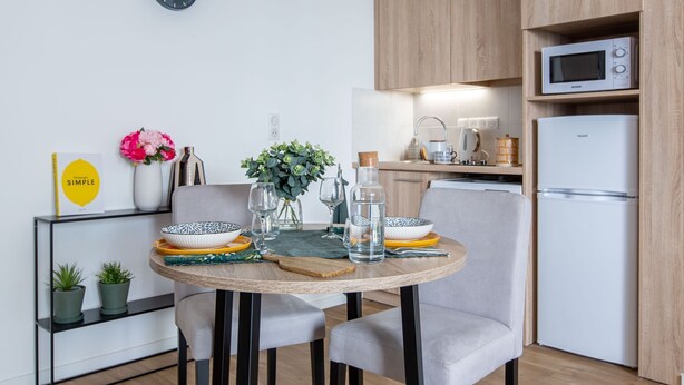 A modern kitchen with a round dining table, chairs, a clock, and built-in appliances. - Zenao Appart'hôtels Tours (Tours)