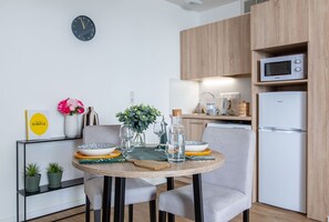 A modern kitchen with a round dining table, chairs, a clock, and built-in appliances. - Zenao Appart'hôtels Tours (Tours)
