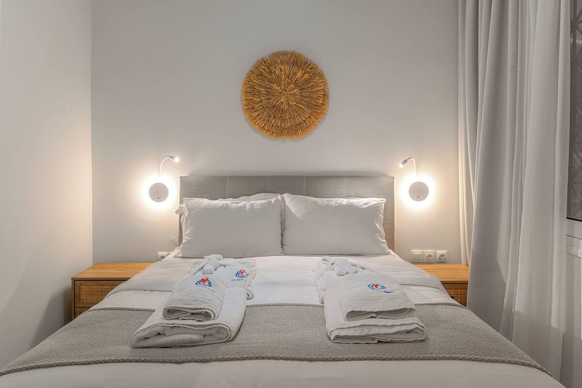 A neatly made bed with towels, a wall-mounted light fixture, and a textured wall decoration.