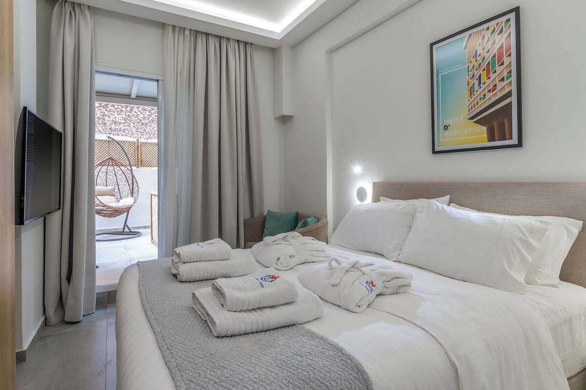 A hotel room with a bed, towels, a television, a chair, and a painting on the wall.