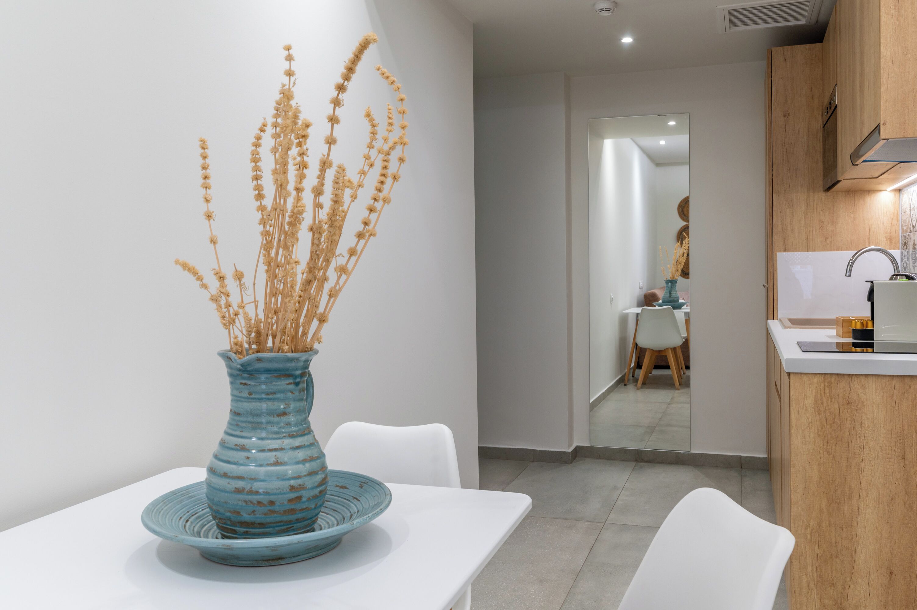 A modern kitchen with a white countertop, a sink, and a blue vase with dried plants on a white table.