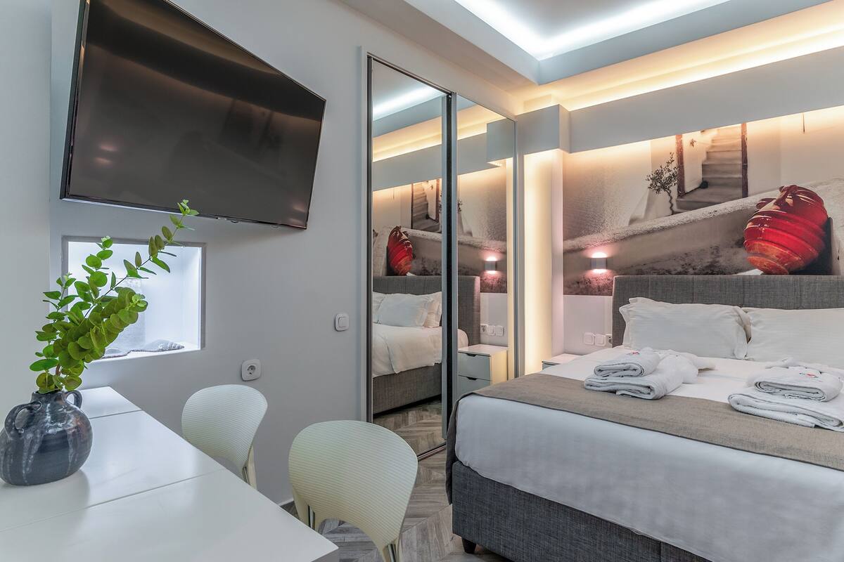 A modern hotel room with a bed, a TV, a desk, and a mirror.