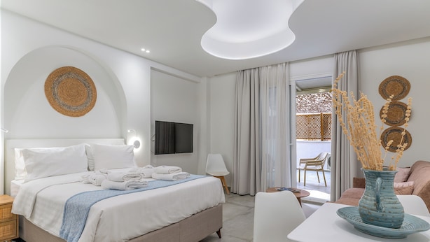 Ett modernt hotellrum med en säng, en platt-TV, ett matbord och en vas med torkade växter.