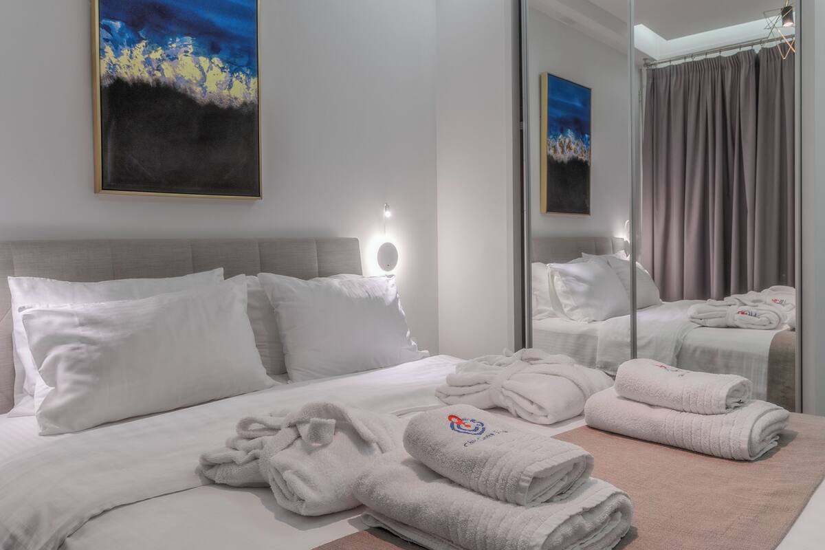 A hotel room with a bed, white towels, a round mirror, and artwork on the wall.