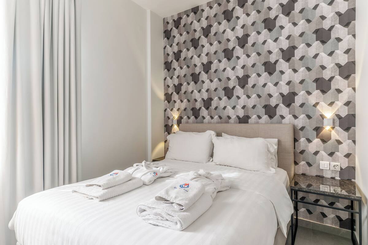 A hotel room with a neatly made bed, a geometric patterned wall, and a bedside table with a lamp.