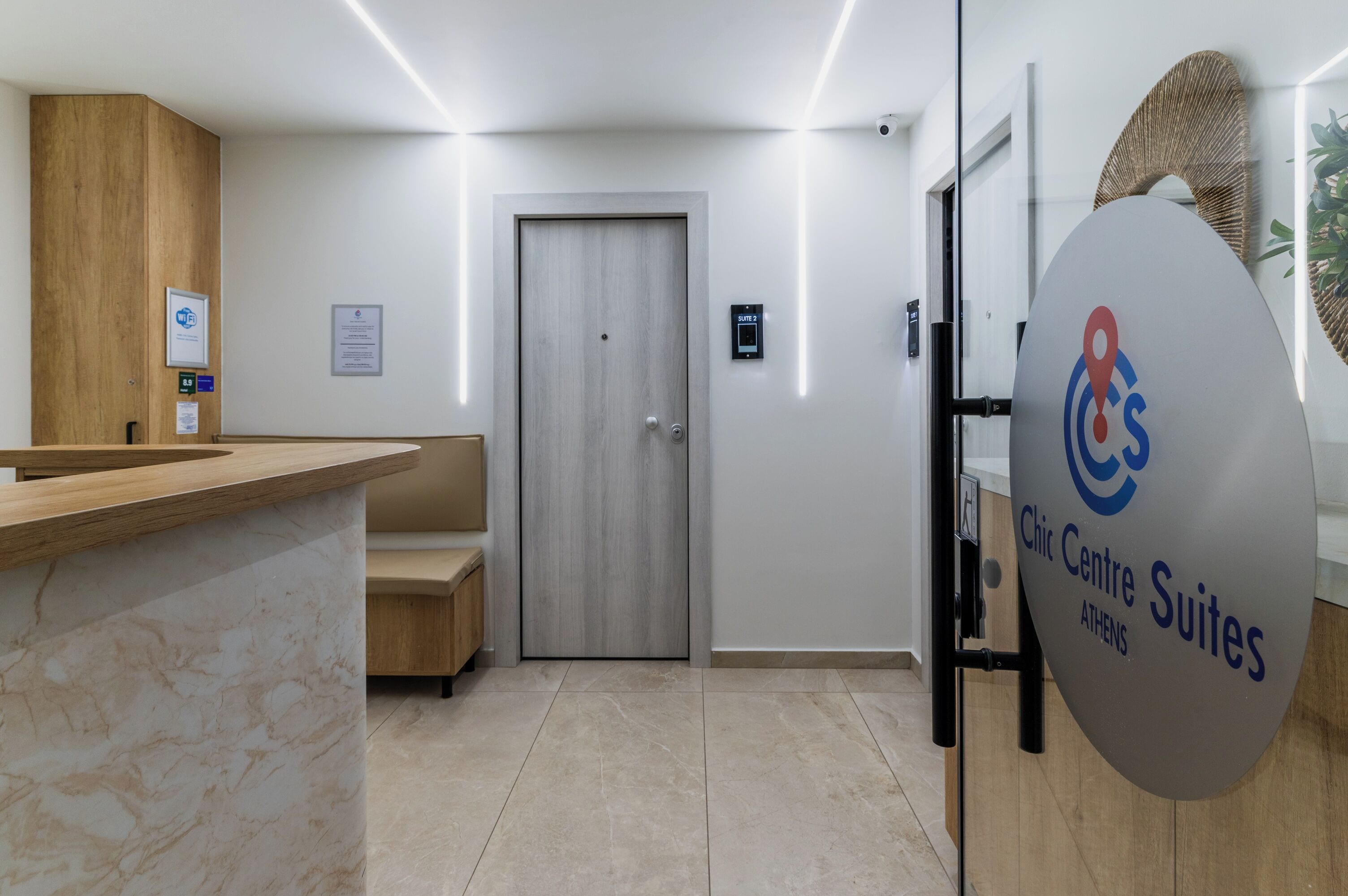 Een receptiebalie, een houten bank, een deur en een bordje met de tekst Chic Centre Suites in Athene.