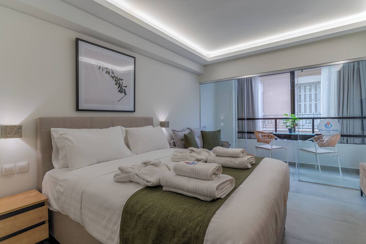 A hotel room with a bed, a desk, a chair, a window with curtains, and a framed picture on the wall.