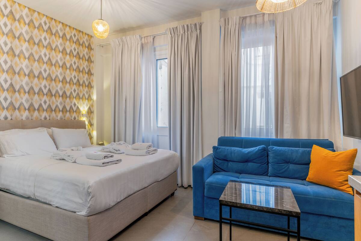 A hotel room with a bed, a blue sofa, a small table, and a TV.