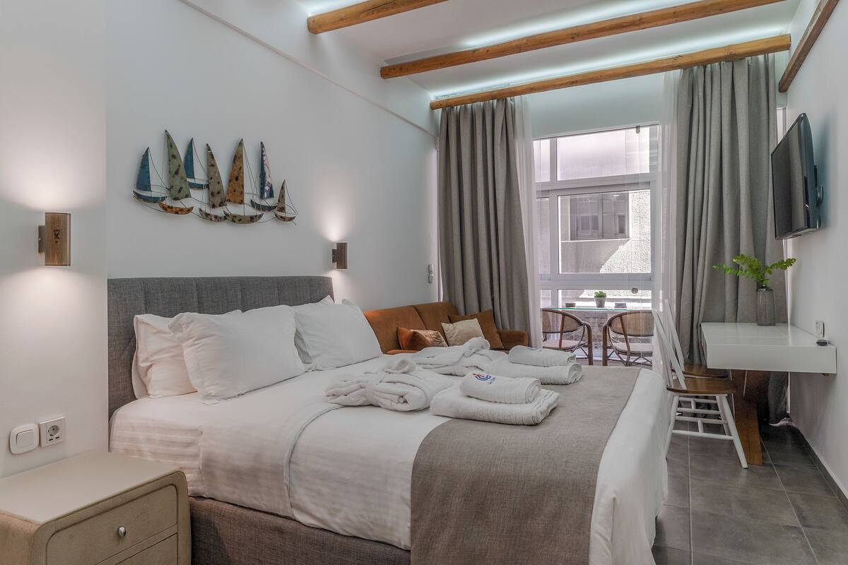 A hotel room with a bed, a desk, a chair, a TV, and a window with curtains.
